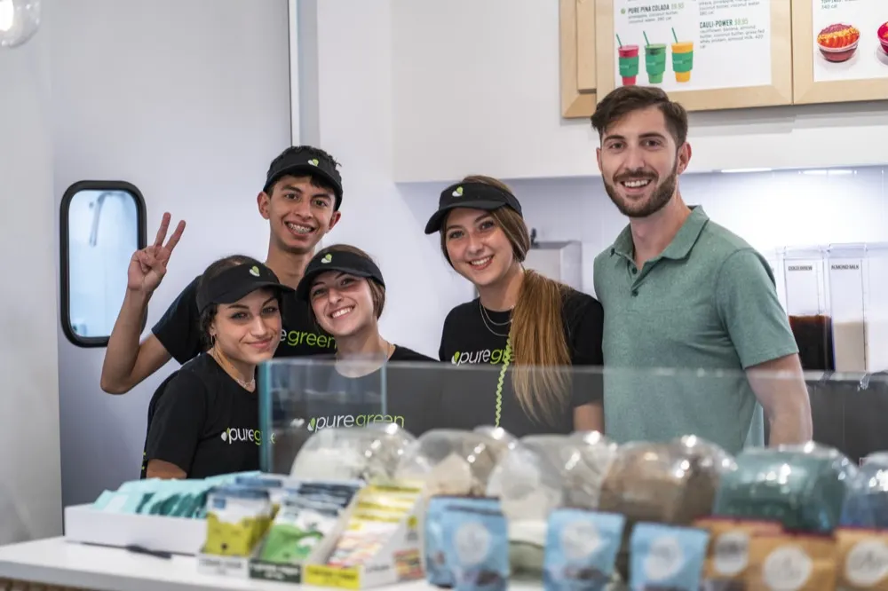 Five smiling Pure Green team members behind the counter